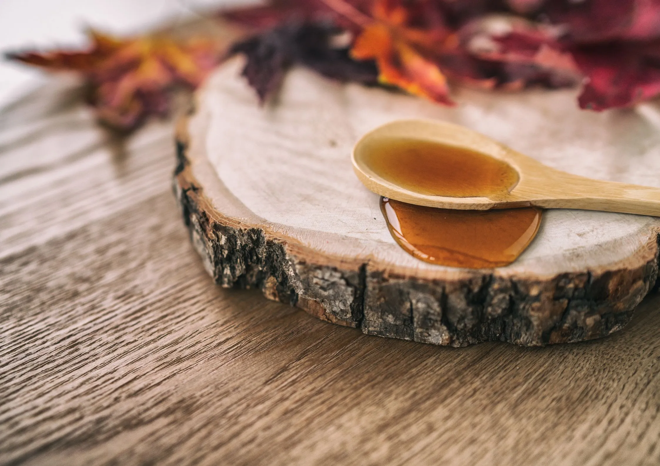 Light amber organic liquid sugar on a wooden spoon with autumn leaves.